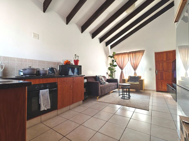 Open-plan living area featuring vaulted ceilings with exposed timber beams, tiled flooring, and a functional kitchen with granite countertops and wood cabinetry.
