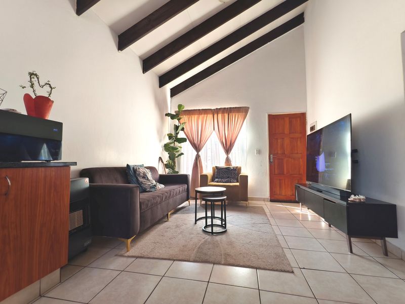 A cozy living room featuring high vaulted ceilings with exposed timber beams, tiled flooring, and a solid timber entrance door.