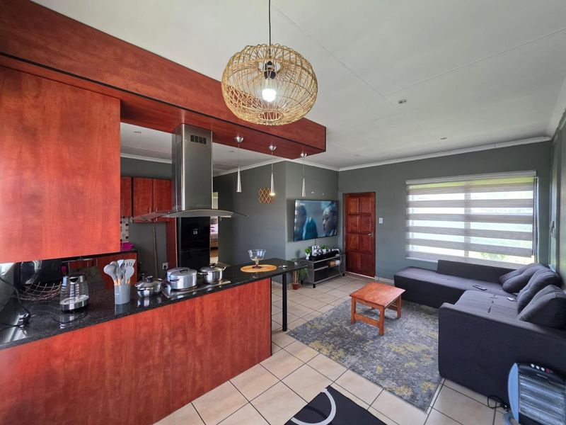 Open-plan living area featuring a modern kitchen with wood-finish cabinetry, granite countertops, stainless steel extractor, and tiled flooring throughout the combined space.