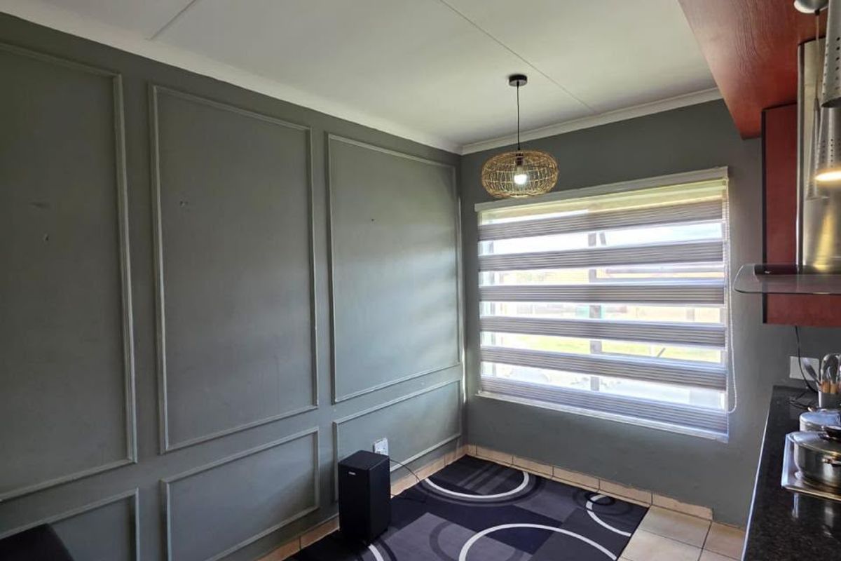 A kitchen area featuring decorative wall paneling, tiled flooring, granite countertops, and modern zebra blinds, providing a functional and stylish space.