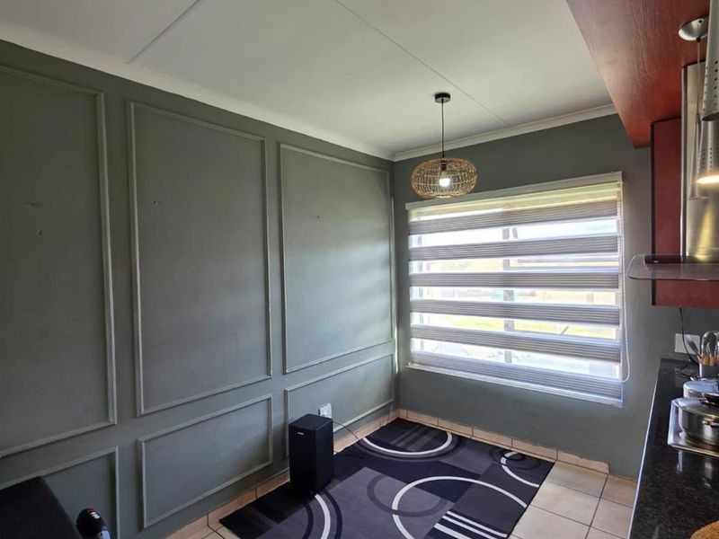 A kitchen area featuring decorative wall paneling, tiled flooring, granite countertops, and modern zebra blinds, providing a functional and stylish space.
