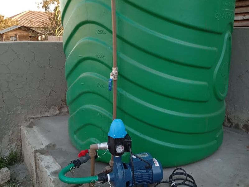 Exterior utility area featuring a large green water storage tank connected to a pressure pump system on a concrete base.