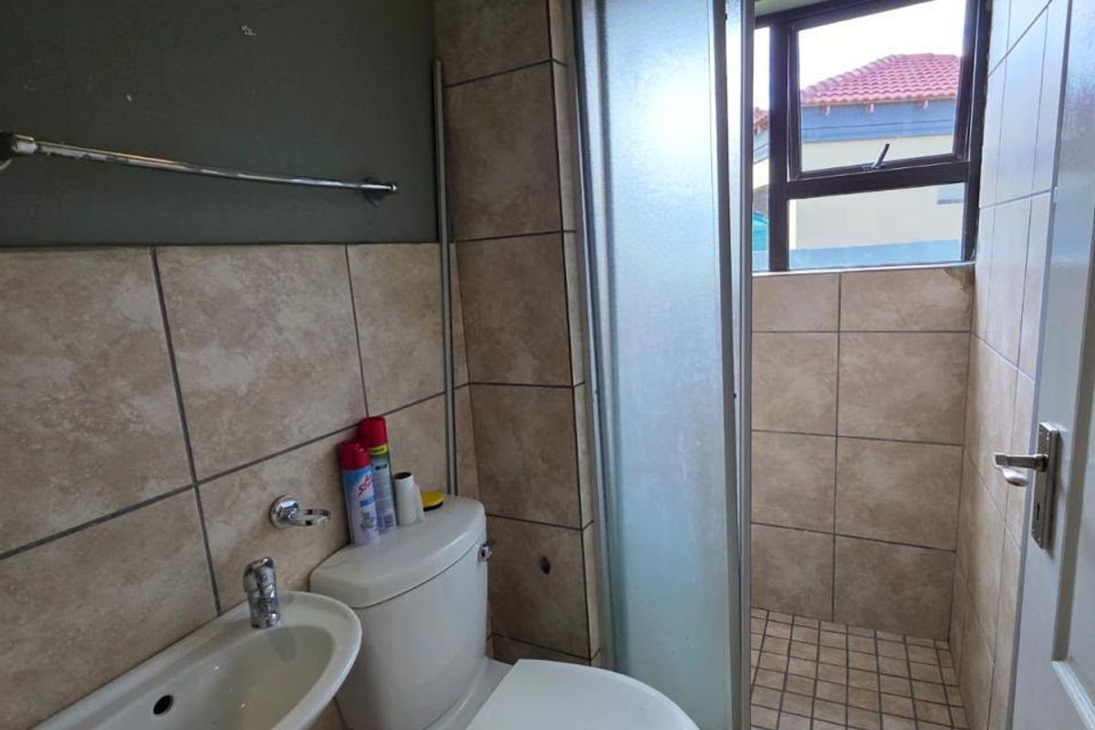 A compact bathroom featuring a wall-mounted basin, toilet, and a tiled shower enclosure with a frosted glass door.