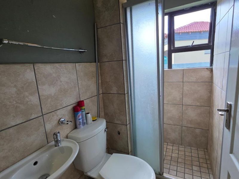 A compact bathroom featuring a wall-mounted basin, toilet, and a tiled shower enclosure with a frosted glass door.