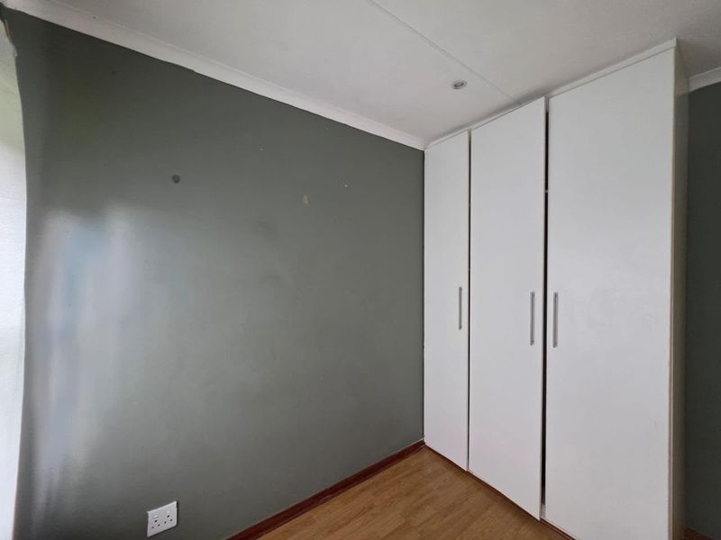 A clean, empty bedroom featuring built-in white cupboards, laminate flooring, and neutral grey wall paint, ready for personalization.