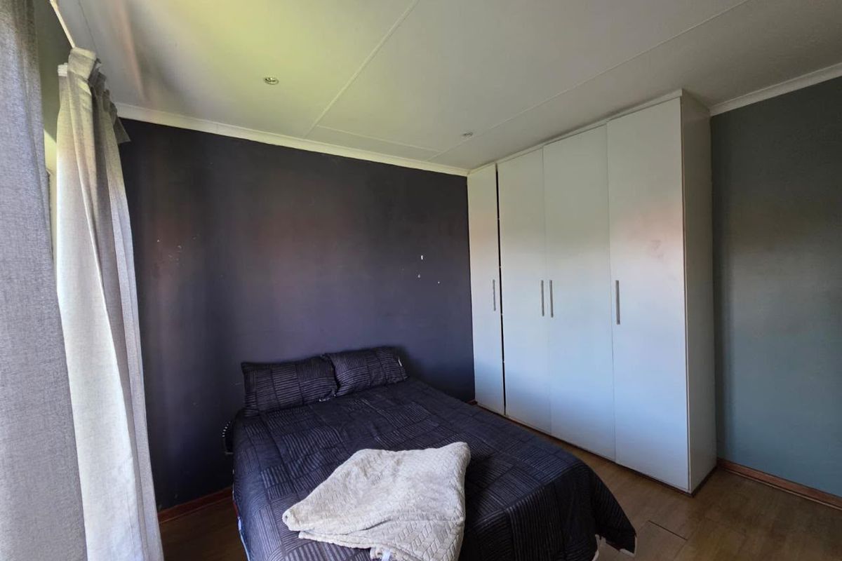 A bedroom featuring laminate flooring, recessed downlighting, and white built-in cupboards with a dark accent wall.
