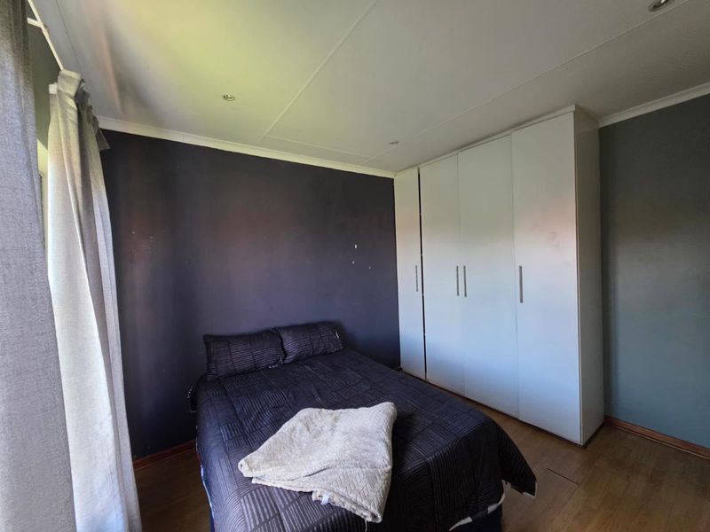A bedroom featuring laminate flooring, recessed downlighting, and white built-in cupboards with a dark accent wall.
