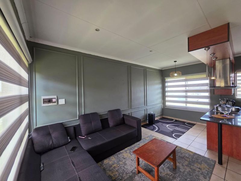 Open-plan living and kitchen area featuring wainscoting, tiled flooring, modern roller blinds, and a functional kitchen with granite countertops and an extractor fan.