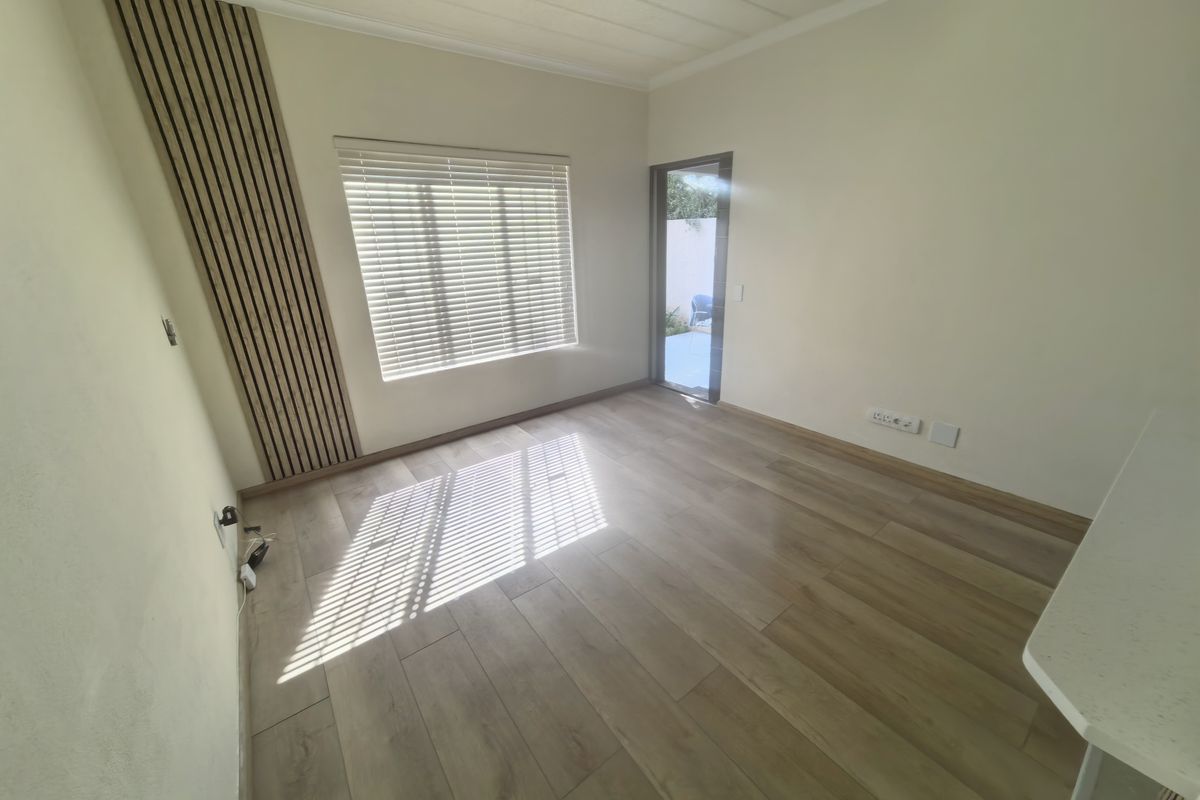 Bright and spacious living area featuring modern wood-look laminate flooring, a stylish slatted timber accent wall, and direct access to an outdoor space.