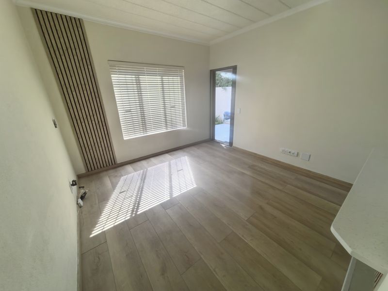Bright and spacious living area featuring modern wood-look laminate flooring, a stylish slatted timber accent wall, and direct access to an outdoor space.