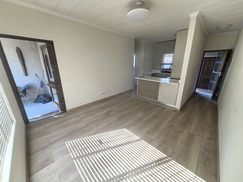 An open-plan living area featuring light laminate flooring, a breakfast bar, and a compact kitchen, with direct access to an outdoor patio area.