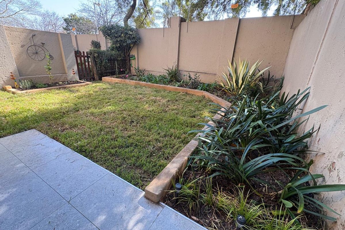 A private rear garden featuring a tiled patio area, raised garden beds, and a secure concrete boundary wall.
