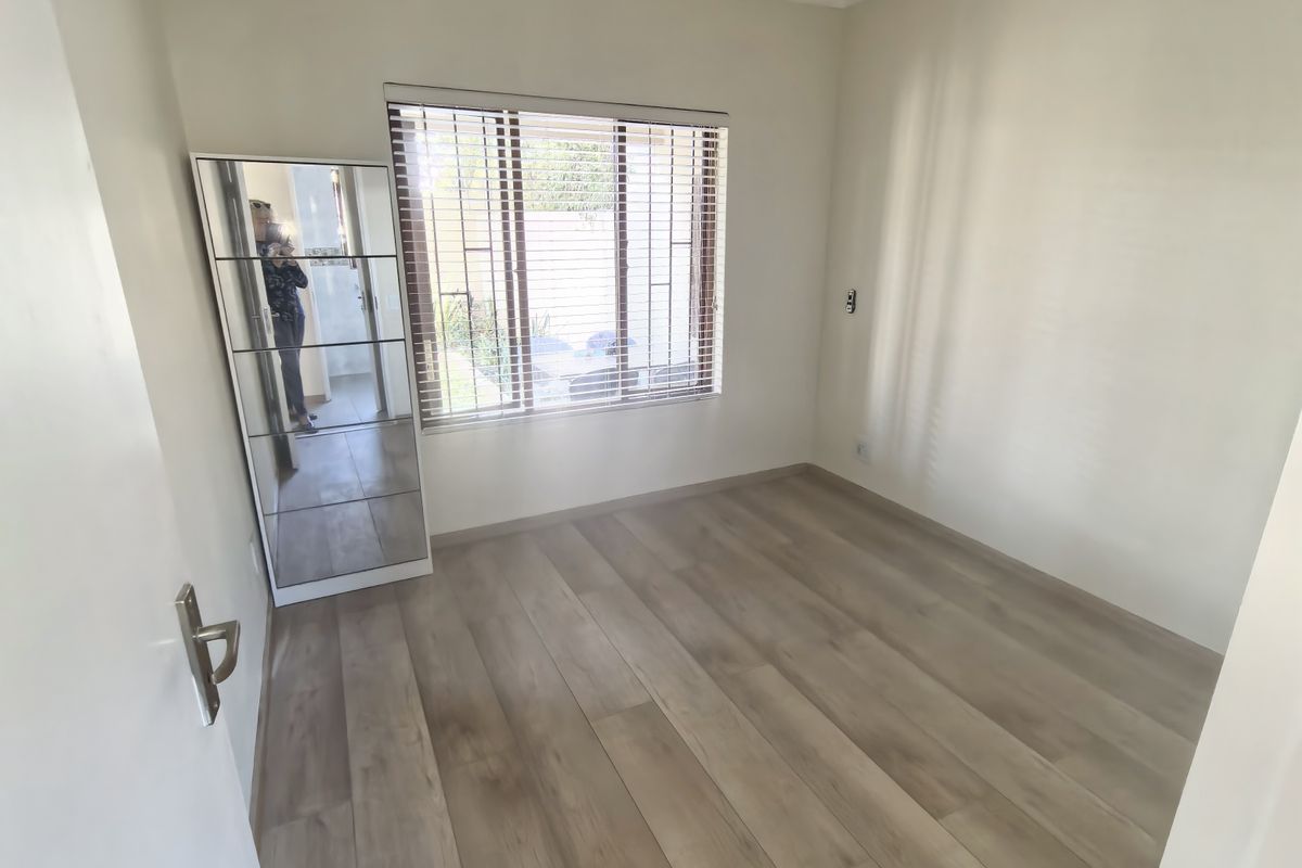 A bright, empty bedroom featuring modern laminate flooring, a ceiling fan, and venetian blinds, offering a clean and neutral space ready for personalization.