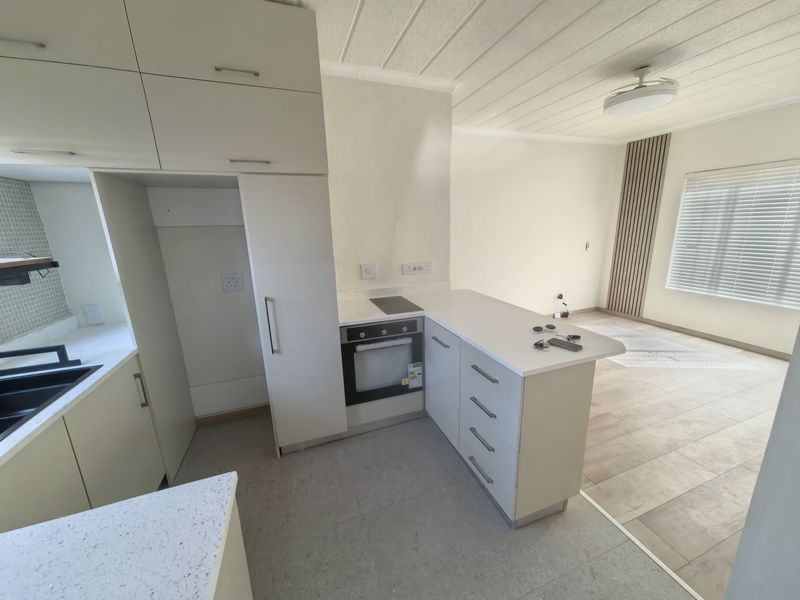Modern open-plan kitchen and living area featuring sleek white cabinetry, quartz countertops, integrated appliances, and contemporary tiled flooring with stylish slat wall accents.