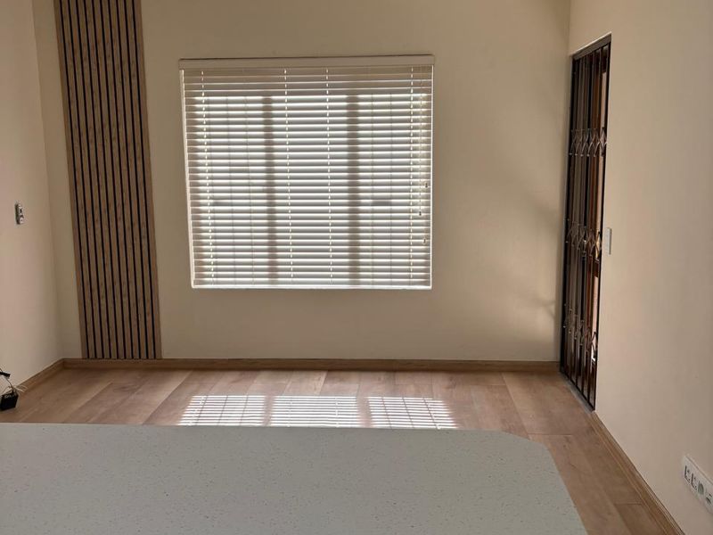 An open-plan living area featuring modern laminate flooring, slatted wood wall accents, a kitchen island, and a security gate leading to the exterior.