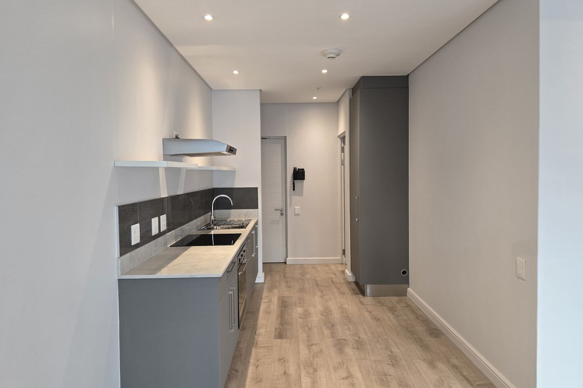 Modern, minimalist kitchen featuring sleek grey cabinetry, stone countertops, integrated hob, and extractor fan, finished with light wood-look laminate flooring and recessed lighting.