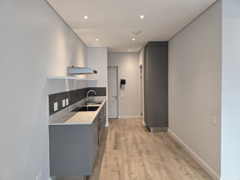 Modern, minimalist kitchen featuring sleek grey cabinetry, stone countertops, integrated hob, and extractor fan, finished with light wood-look laminate flooring and recessed lighting.