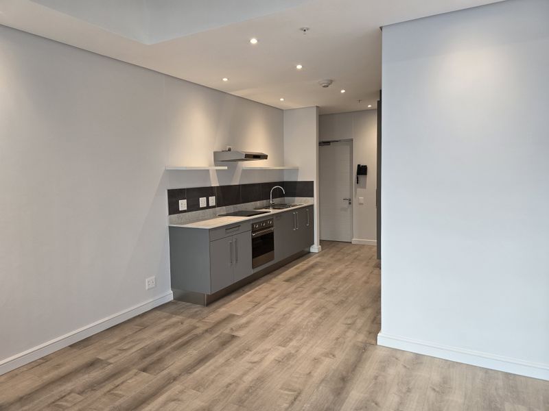 A modern, minimalist kitchen featuring grey cabinetry, integrated appliances, a tiled splashback, and wood-look laminate flooring in an open-plan layout.