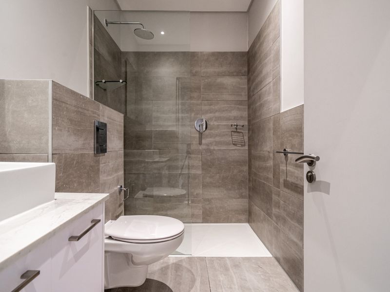 Modern bathroom featuring a walk-in shower with glass screen, wall-mounted toilet, and a sleek vanity with stone countertop and basin.