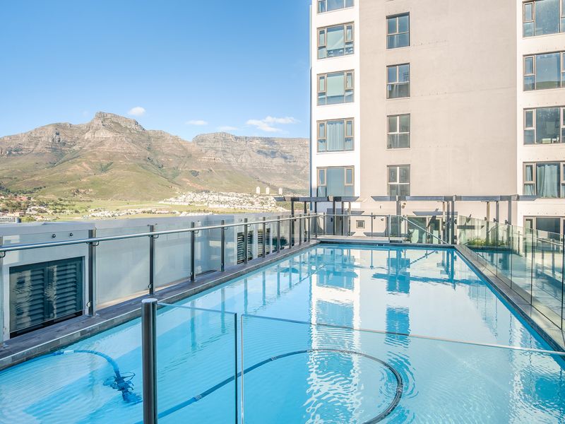 A well-maintained rooftop swimming pool featuring glass balustrades and stunning mountain views, set within a modern apartment complex.