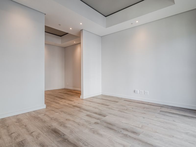 A bright, modern, and empty living area featuring recessed ceiling details, recessed lighting, and high-quality laminate wood flooring throughout.