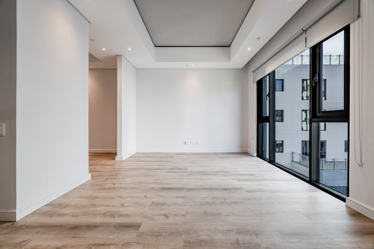 A bright, modern, and empty living area featuring high-quality laminate flooring, a stylish recessed ceiling, and large windows providing ample natural light.