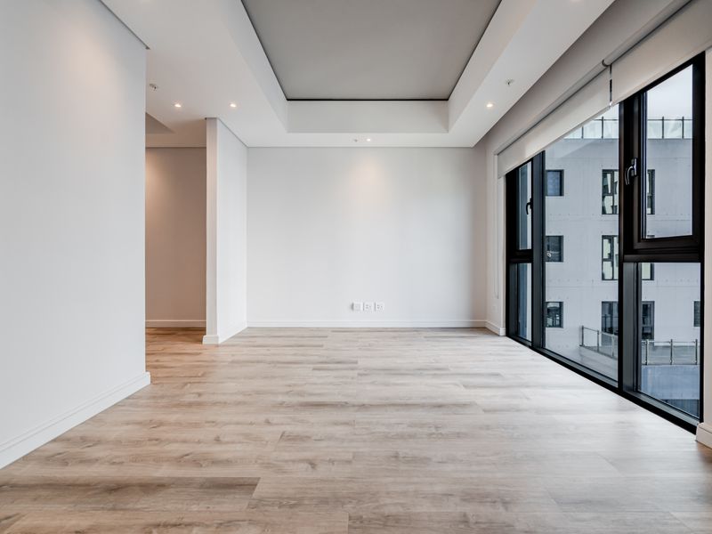 A bright, modern, and empty living area featuring high-quality laminate flooring, a stylish recessed ceiling, and large windows providing ample natural light.