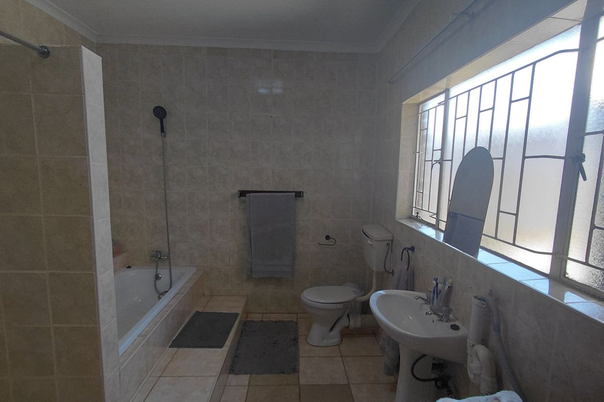 A functional bathroom featuring a built-in bathtub, pedestal sink, and toilet, finished with neutral wall and floor tiles.