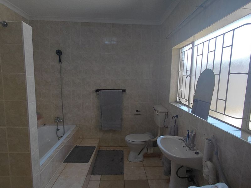 A functional bathroom featuring a built-in bathtub, pedestal sink, and toilet, finished with neutral wall and floor tiles.