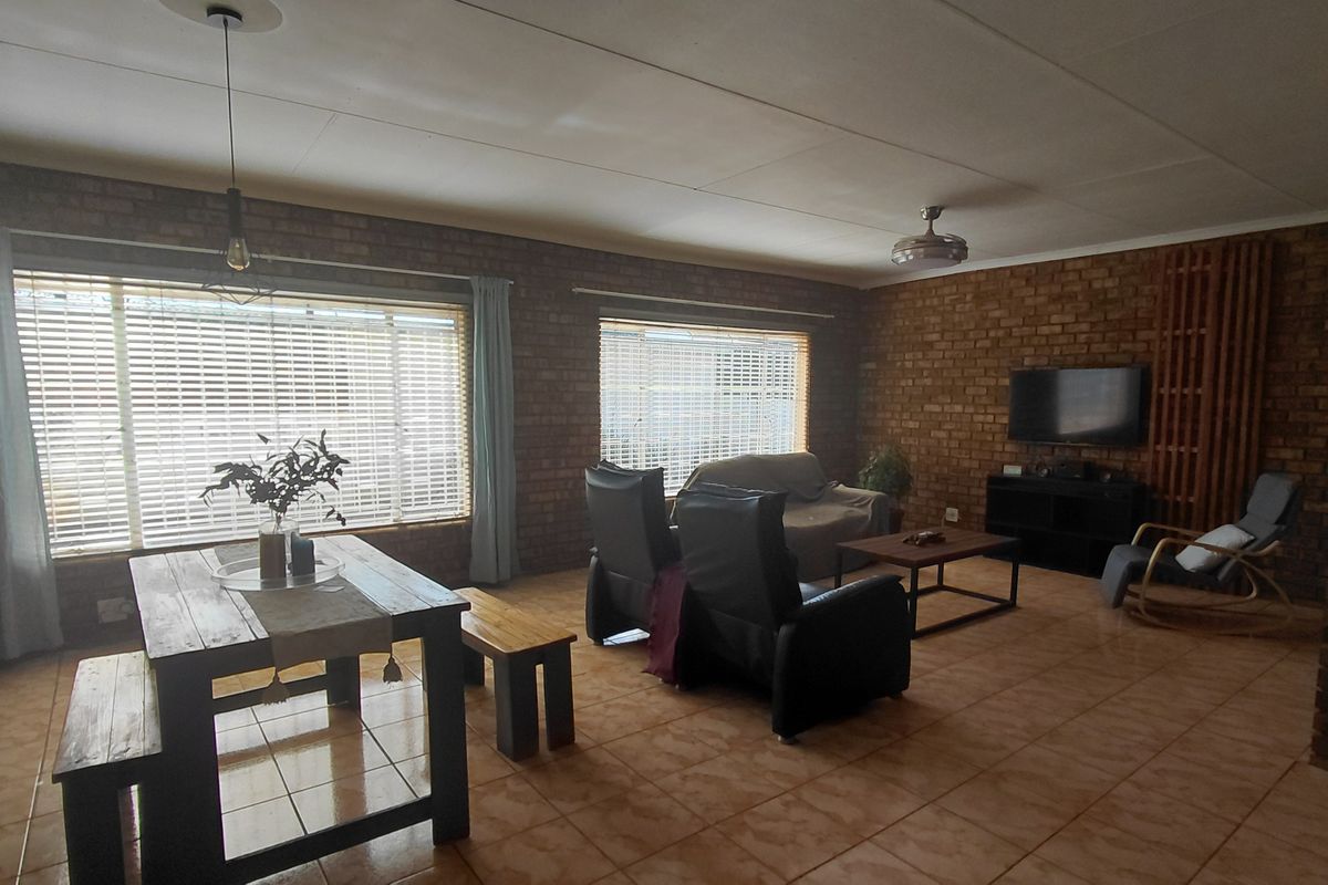 Spacious open-plan living and dining area featuring exposed brick walls, tiled flooring, and large windows allowing for ample natural light.
