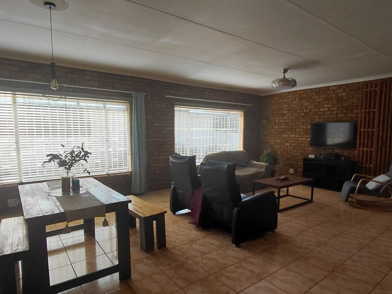 Spacious open-plan living and dining area featuring exposed brick walls, tiled flooring, and large windows allowing for ample natural light.
