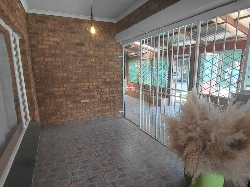 A covered patio area featuring exposed brick walls, tiled flooring, and a security gate, providing a functional outdoor space.