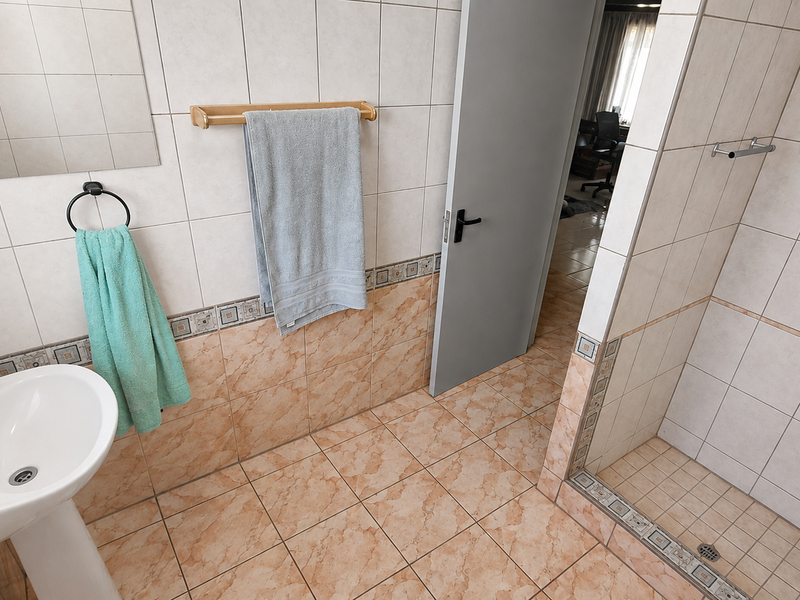 A functional bathroom featuring a pedestal basin, tiled walls and flooring, and a walk-in shower enclosure.