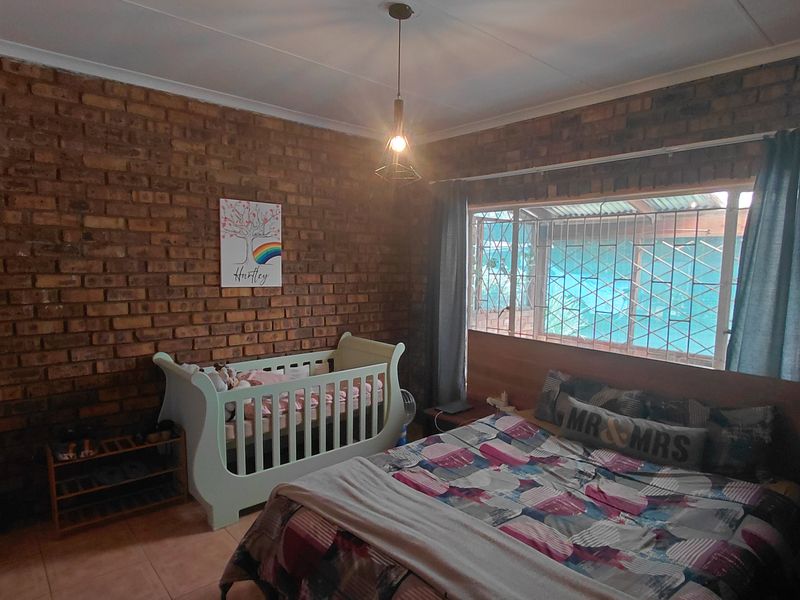 A bedroom featuring an exposed brick feature wall, tiled flooring, and a window fitted with security bars.