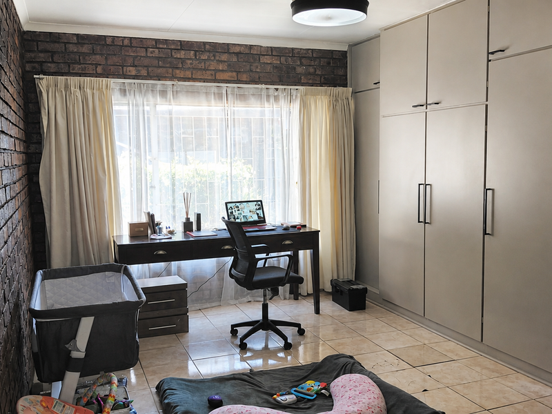A bedroom featuring an exposed brick feature wall, tiled flooring, and extensive built-in cupboard storage.
