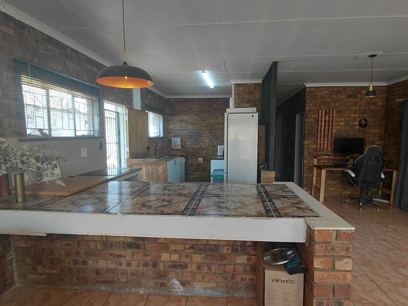 Open plan living and kitchen area featuring exposed brick walls, tiled breakfast bar, and tiled flooring throughout.