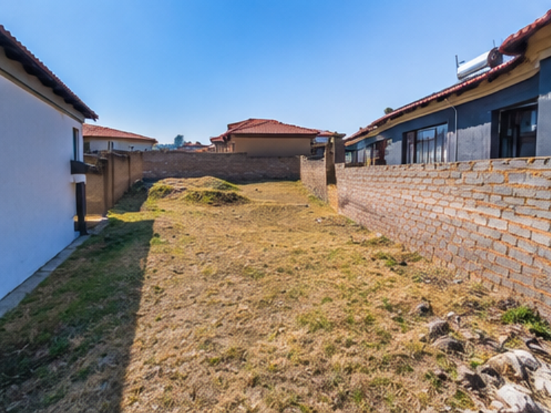 A view of the rear yard area featuring boundary walls and uneven terrain, situated between neighboring residential properties.