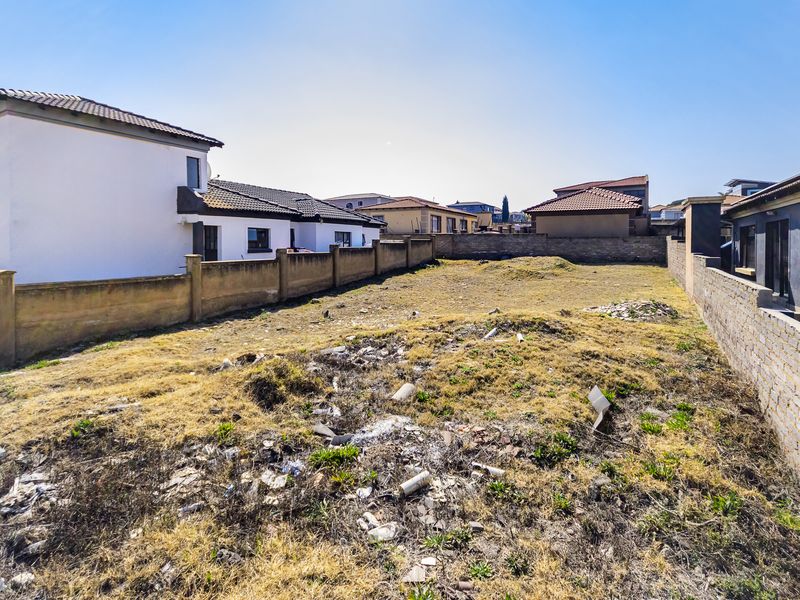 A vacant residential plot enclosed by perimeter boundary walls, featuring uneven terrain and requiring site clearing.