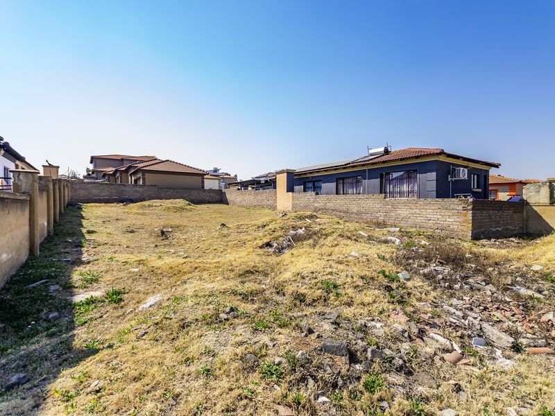 A vacant residential plot enclosed by perimeter brick boundary walls, featuring uneven terrain and scattered debris.