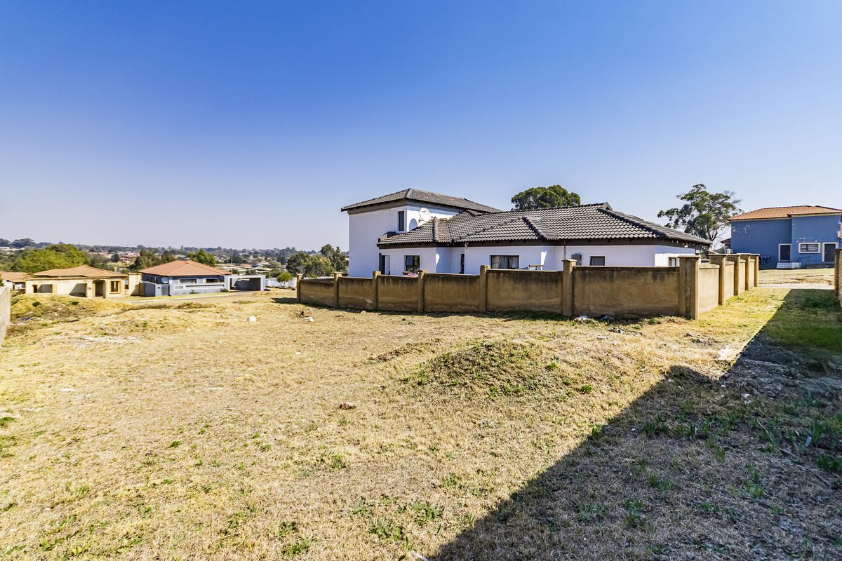 A view of a vacant residential plot with a boundary wall and neighboring house in the background.