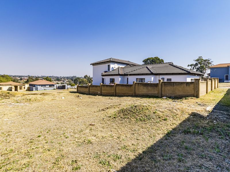 A view of a vacant residential plot with a boundary wall and neighboring house in the background.