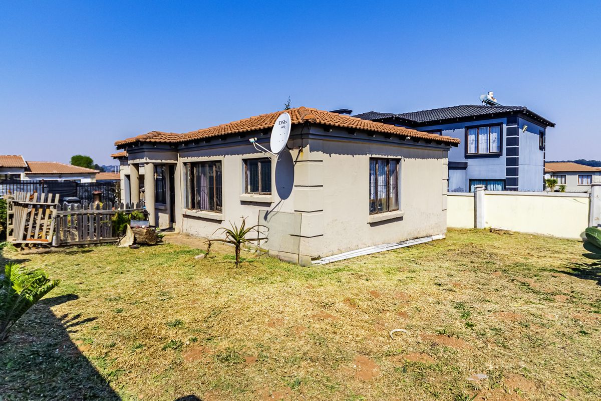 Rear view of a single-story residential house featuring a tiled roof, plastered exterior walls, and a surrounding garden area.