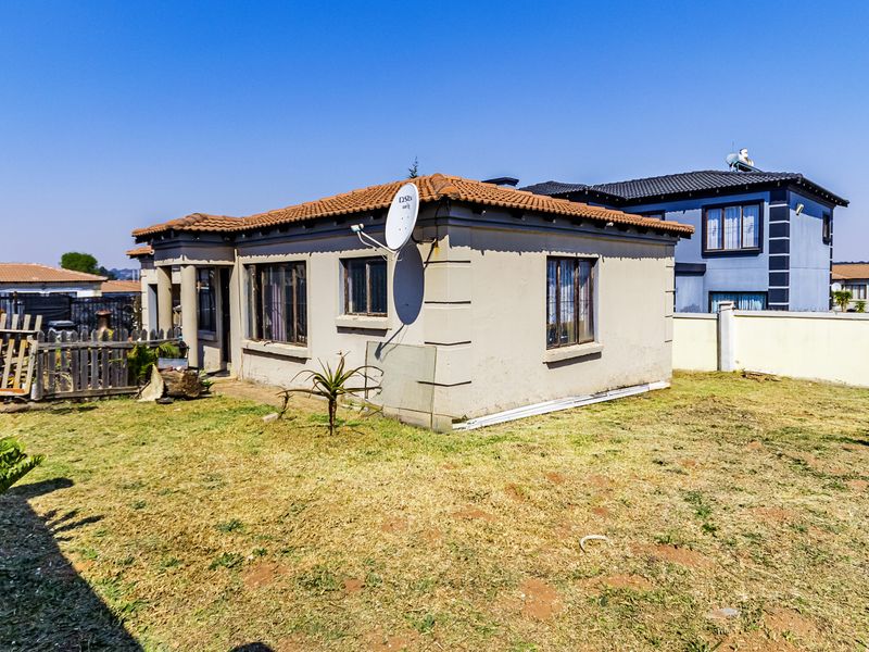 Rear view of a single-story residential house featuring a tiled roof, plastered exterior walls, and a surrounding garden area.