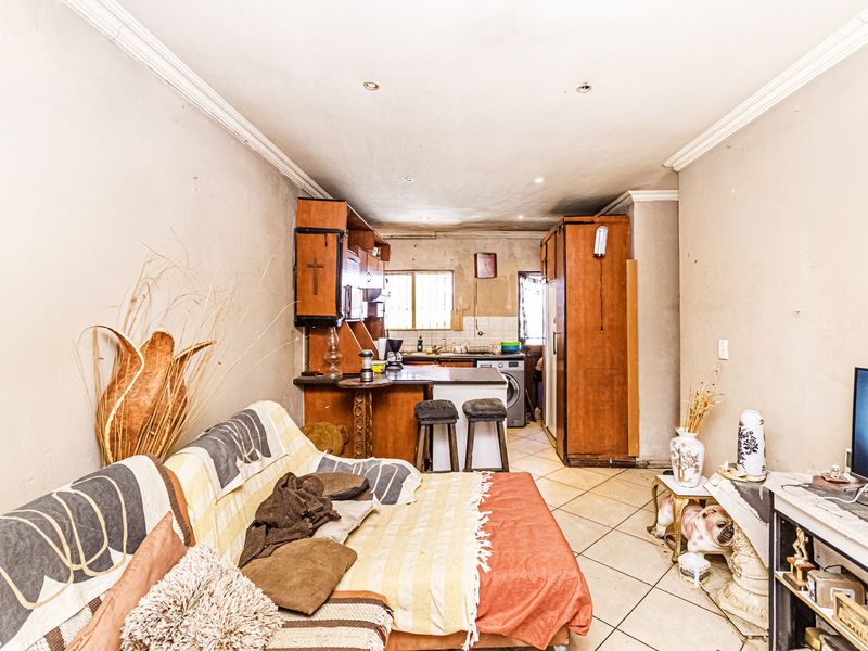 Open-plan living and kitchen area featuring tiled flooring, built-in cabinetry, and a breakfast bar, offering a functional layout with potential for modernization.