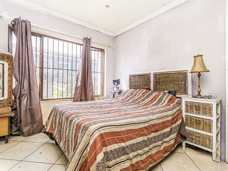 A bedroom featuring tiled flooring, security bars on the window, and recessed lighting, currently requiring cosmetic updates to the wall finishes.