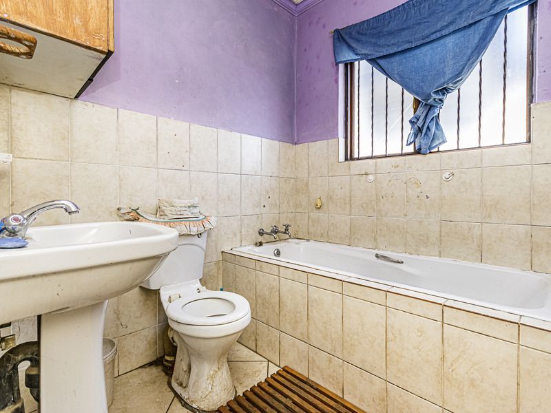 A dated bathroom featuring a pedestal basin, toilet, and built-in bathtub with tiled walls, requiring renovation to update finishes and fixtures.