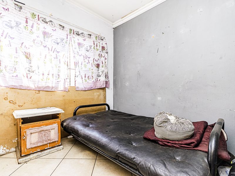 A bedroom featuring tiled flooring and cornicing, currently requiring significant wall repairs and cosmetic updates to improve the overall condition of the space.