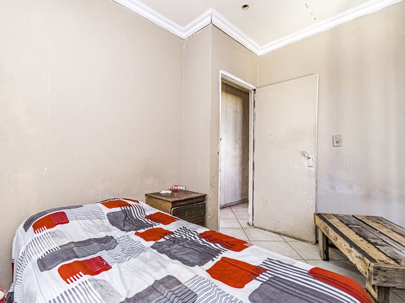 A bedroom featuring tiled flooring, coving, and recessed lighting, currently requiring cosmetic updates to the wall finishes and general maintenance.