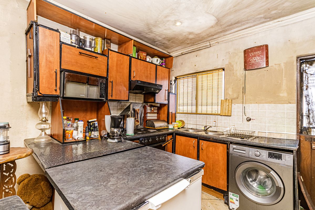 A dated kitchen featuring built-in cabinetry, laminate countertops, and a tiled backsplash, currently requiring significant cosmetic renovation and repair to the ceiling and walls.