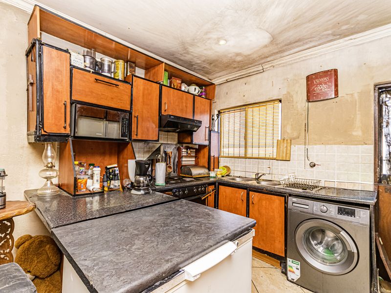 A dated kitchen featuring built-in cabinetry, laminate countertops, and a tiled backsplash, currently requiring significant cosmetic renovation and repair to the ceiling and walls.